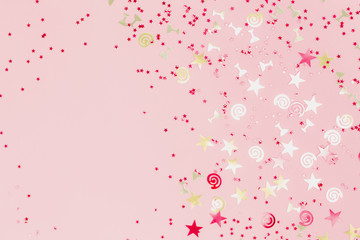 Golden stars flutes and swirls glitter and assorted sparkling confetti partially blurred on trendy pink background. Festive holiday pastel backdrop with blank copy space. selective focus