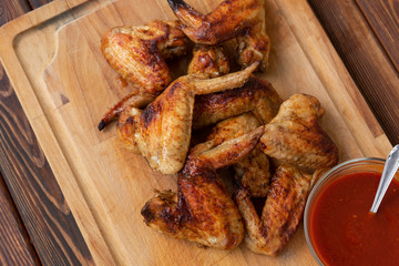 Roasted hot chicken wings on a wooden dish with tomato sauce. Top view