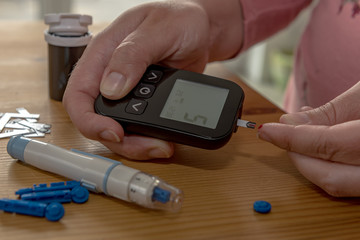 A young woman at home checks her blood sugar with a glucometer and test strips. Concept: Healthcare, people and medicine