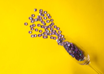 Champagne glass with purple floral confetti on yellow background. Minimal style. Summer or spring party concept.