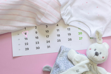 Set of newborn accessories in anticipation of  child - calendar with circled number 8 (eight), baby clothes, toys on pink background. Copy space, flat lay, top view.