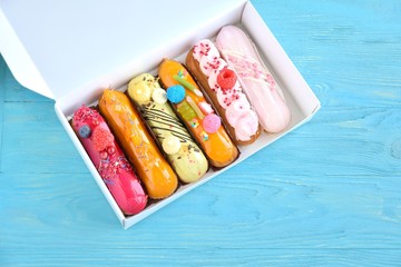 Beautiful delicious french eclairs set with original cream decor in white box on blue wooden...