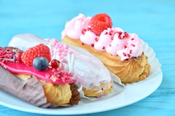 Traditional french eclairs with pink strawberry cream and creative berries decor on blue wooden table. Selective focus. Delicious dessert profiteroles with original decor. Three tasty eclair