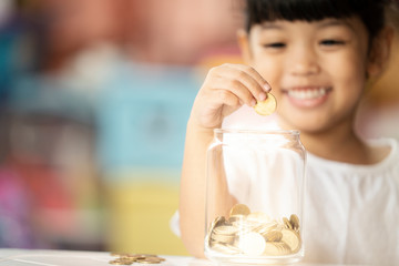 Kid dropping coins into the glass for saving the money. Selective focus