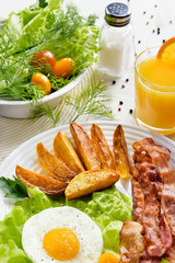 French fries and egg with bacon on top in a white bowl, on a large table with greens.