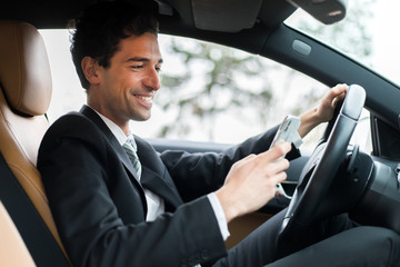 Businessman ignoring safety and texting on mobile phone while driving