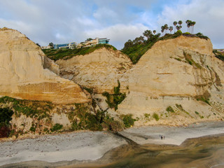 Aerial view of pacific coastline with yellow sandstone cliffs and waves rushing the beach during sunset. Black Beach, Torrey Pines State Natural Reserve, San Diego, California, USA