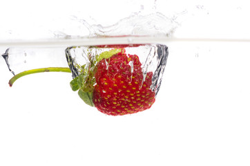 Red fresh strawberries thrown into the water, under water. Spat and splash