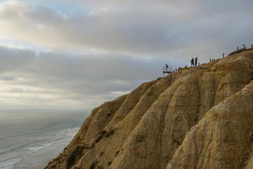 Aerial view of pacific coastline with yellow sandstone cliffs and waves rushing the beach during sunset. Black Beach, Torrey Pines State Natural Reserve, San Diego, California, USA