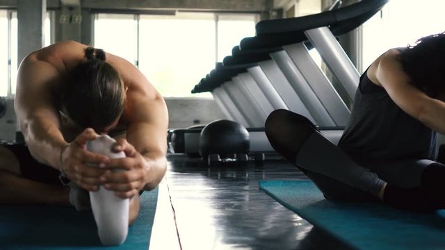 Young woman and man stretching their legs on the gym floor. Two people couple working out indoors