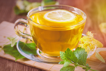 A cup with fragrant lime tea, standing on a wooden table, in the rays of sunlight.