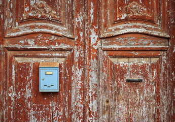 Una puerta descolorida y antigua de madera, en color rojo, con un buzón metálico azul