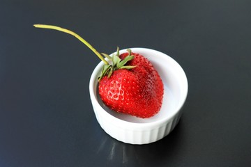Fresh red strawberries in ceramic bowl on dark background. First harvest of ripe strawberries on plate. Strawberries with strawberry leaf on dark background.