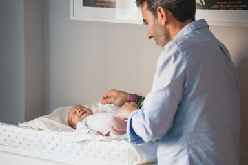 New father changing the diaper to his cute newborn. Baby expresses calm and peace. Social and Gender equality. Family, new life, childhood, fatherhood concept.