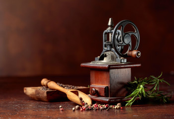 Old pepper mill with cooking utensils,various peppers and rosemary on a brown background.