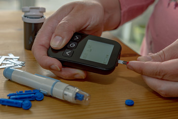 A young woman at home checks her blood sugar with a glucometer and test strips. Concept: Healthcare, people and medicine