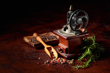 Old pepper mill with cooking utensils,various peppers and rosemary on a brown background.