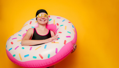 Photo of happy girl in swimming goggles, swimsuit with donut life buoy on empty orange background