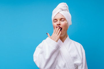 Photo of yawning woman in white coat and towel on head