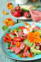 salad with nasturtium flowers and leaves with strawberries and avocados. dressed with strawberry vinaigrette or strawberry dressing with poppy seeds. bright summer salad with edible flowers.