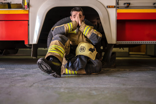 Picture of tired fireman sitting on floor near red fire truck
