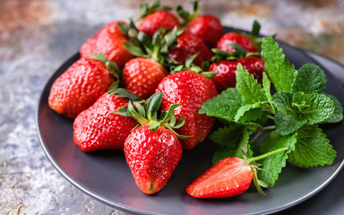 Ripe strawberries and mint on the shade plate on rusty background. Close Up
