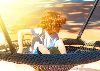 Cheerful boy swinging in the swing-nest. Entertainment for preschoolers outdoors