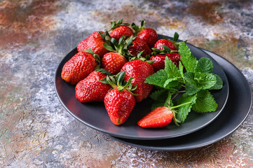 Strawberries and mint on the shade plate on rusty background.