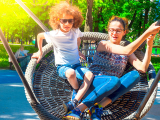 Little laughing family of two children swing on swing. Happy childchood concept image.
