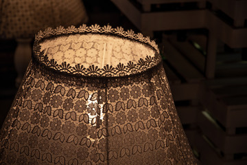 Vintage lace lampshade closeup in darkness. Shabby chic lamp decor. Retro lamp decorated with...