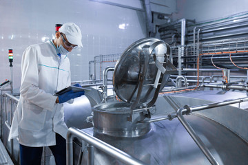 Inspector in a mask and a scrub stands with a folder-tablet in his hands at the dairy plant