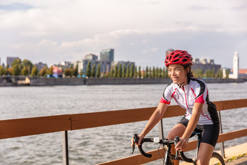 Urban biking girl riding road bike cycling in the city. Happy cyclist with downtown background by...