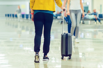 A girl walks through the airport hall and carries a suitcase on wheels. Vacation travel