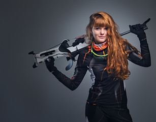 Redhead female Biathlon champion aiming with a competitive gun in a studio over grey...