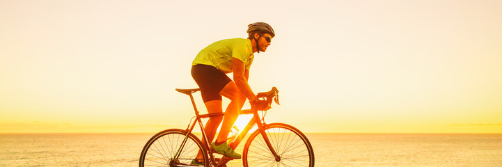 Triahtlon athlete man biking on road racing bike ride outdoors at sunset banner panorama landscape....