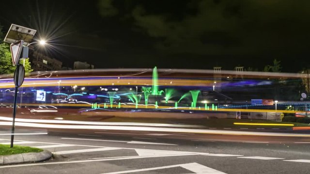Hyper Lapse alrededor de fuente en ciudad con trafico circulando y senderos de luz durante la noche
