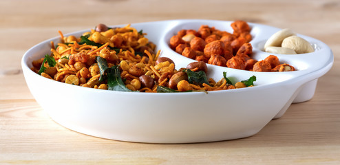 Assortment salty crunchy indian mix Nimco or Namkeen and spicy coated peanut white bowl wooden background.