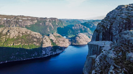 A view from an edge of a cliff to the famous Preikestolen. First sunbeams are appearing in the fjord valley. Great view on Lysefjorden. Dangerous and demanding hike.