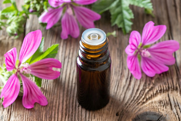 A bottle of mallow essential oil with fresh malva sylvestris flowers