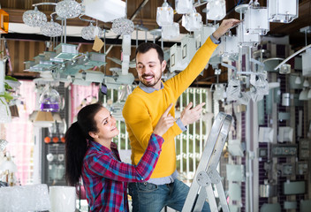 man and girl in lighter shop choosing modern round glass ceiling lamp for house