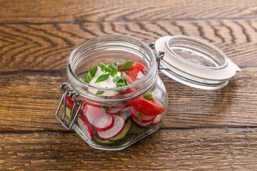 healthy salad with fresh tomato, cucumber, radish in jar isolated on wooden background