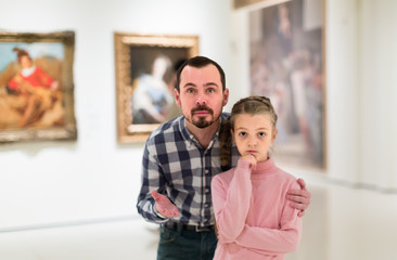 cheerful father and daughter regarding paintings in museum