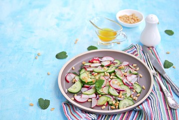 Light salad of crispy radish, cucumber and mint leaves with citrus dressing on a brown plate. Sprinkled with pine nuts.