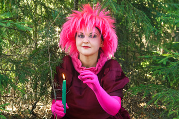 Young witch in purple clothes with a candle in his hand in the forest.