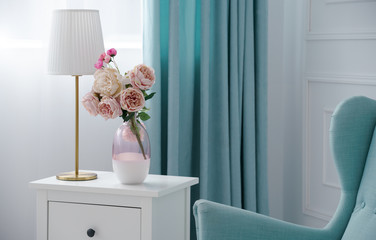 Flower vase and golden table lamp with blue armchair and curtains