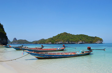 Fototapeta na wymiar Boats near the beach in Ang Thong National Park on the background of an island with trees and blue sky and sea.
