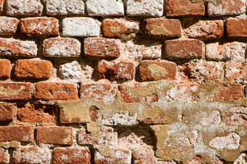 Background of old red brick. The wall of the old house without plaster. Brick is a durable material, but it collapses without a protective layer of plaster. Then the whole wall collapses.