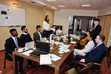 Fototapeta na wymiar Multiracial business team meeting around boardroom table, two team leaders throw paper up.