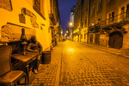 Sculpture of man sitting at table at night in Lviv, Ukraine