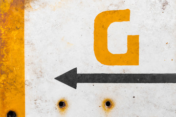 Painted orange letter g and a black arrow on a dirty rusty metal surface with holes